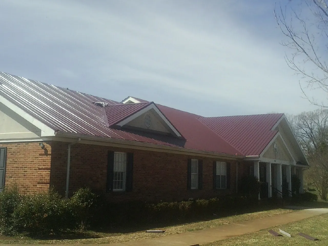 Red metal roof with gabled entries on a long brick building, from a Hail Damage Roof Repair job in Opolis