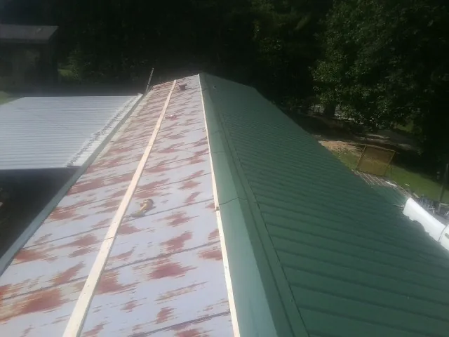 Old rusted panels beside newly installed green metal roofing — Wind Damage Roof Repair by Roofing Brothers in Opolis