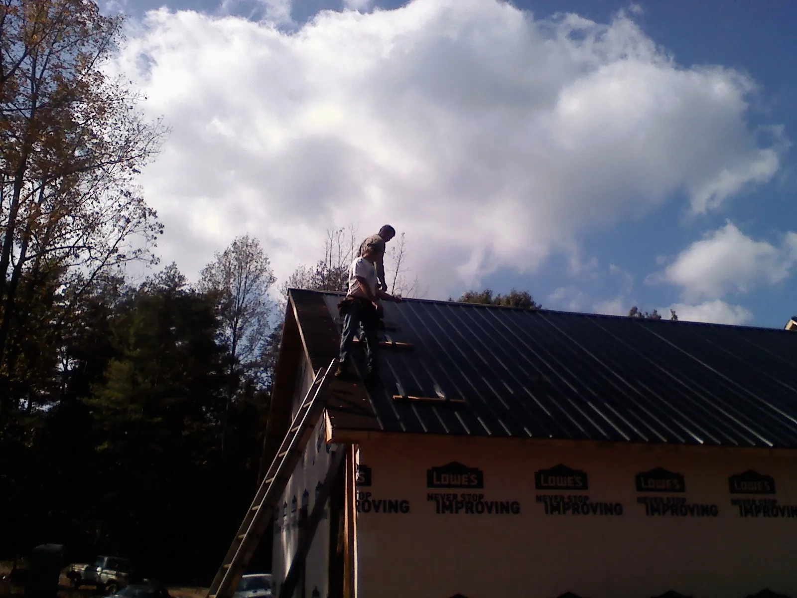 Roofer fastening dark metal panels high against a cloudy sky, from a Roof Inspection job in Opolis