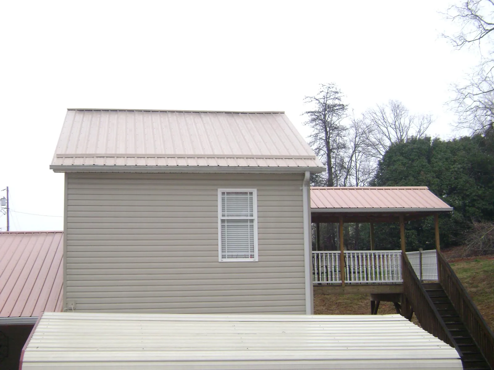 Tan metal roofs on a two story addition and attached porch, from a Roof Replacement job in Opolis
